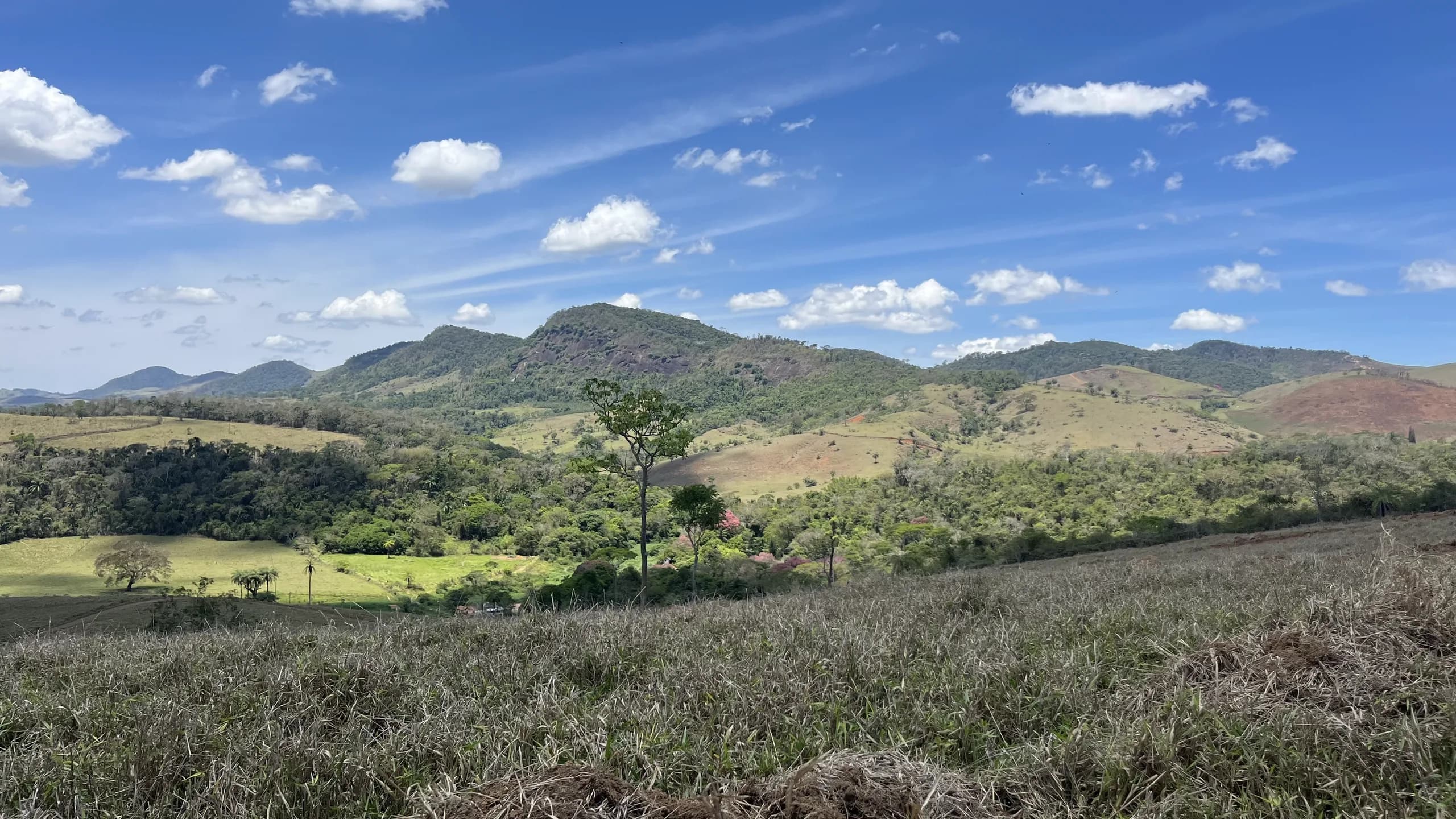 Fotografia real do vale em Matias Barbosa: montanhas verdes e céu azul com nuvens